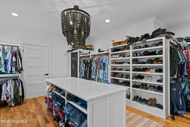 spacious closet with light wood finished floors and an inviting chandelier