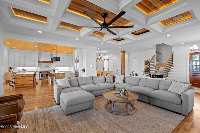 living room with ornamental molding, beam ceiling, light wood-style flooring, and stairway