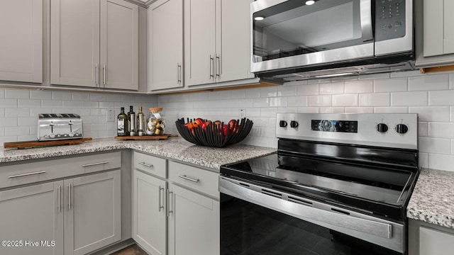 kitchen with light stone countertops, gray cabinets, stainless steel appliances, and decorative backsplash