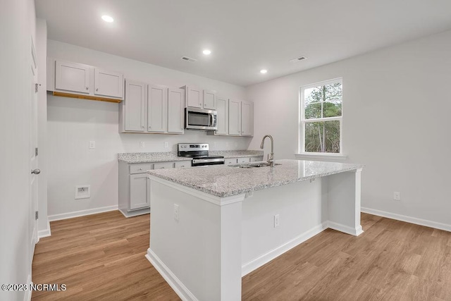 kitchen with an island with sink, recessed lighting, light wood-style flooring, stainless steel appliances, and a sink