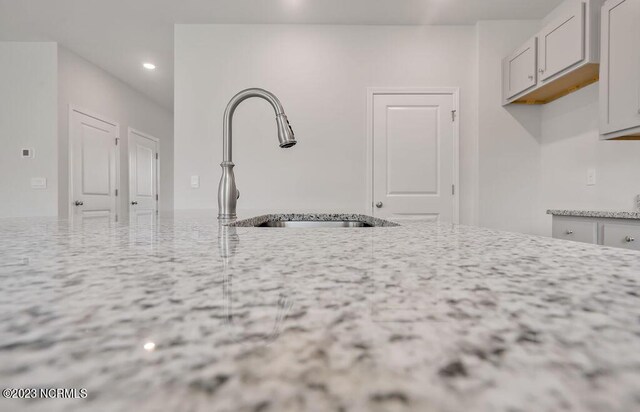 kitchen with a sink, light stone counters, and recessed lighting