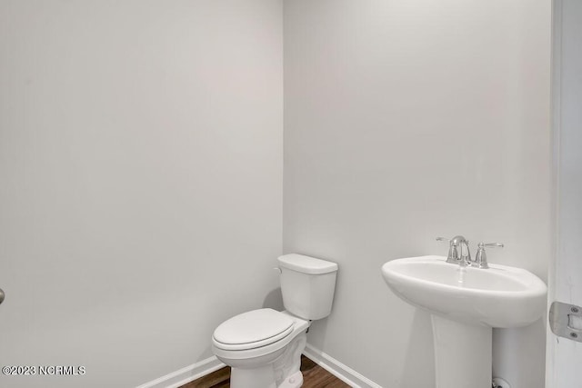 half bath with toilet, wood finished floors, baseboards, and a sink