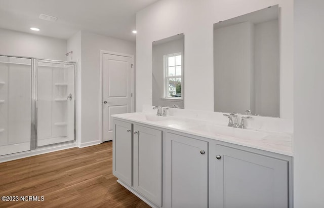 full bath featuring double vanity, wood finished floors, a stall shower, and a sink