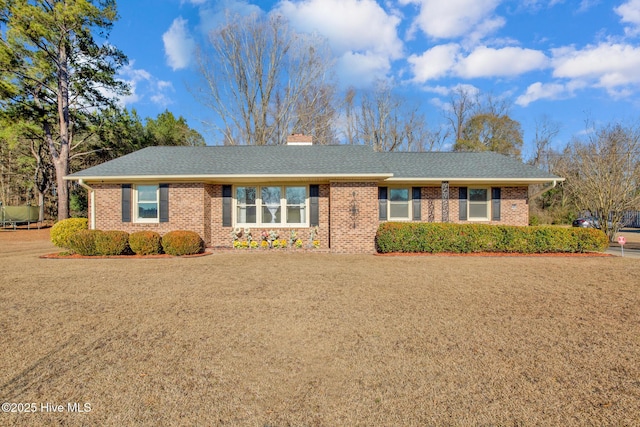 ranch-style home featuring roof with shingles, a chimney, a front lawn, and brick siding