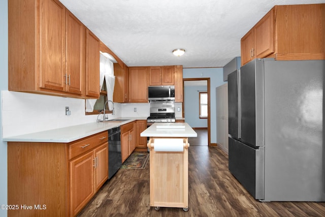 kitchen featuring dark wood finished floors, a kitchen island, stainless steel appliances, light countertops, and a sink