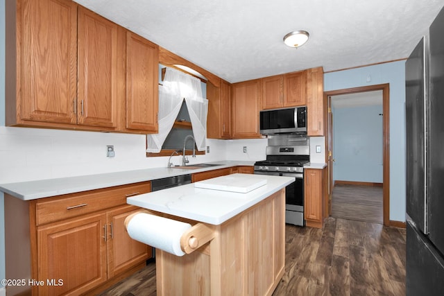 kitchen with stainless steel appliances, a kitchen island, a sink, light countertops, and dark wood-style floors