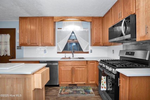 kitchen with crown molding, stainless steel appliances, light countertops, a sink, and a textured ceiling