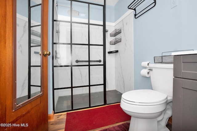 bathroom with wood finished floors, a marble finish shower, and toilet