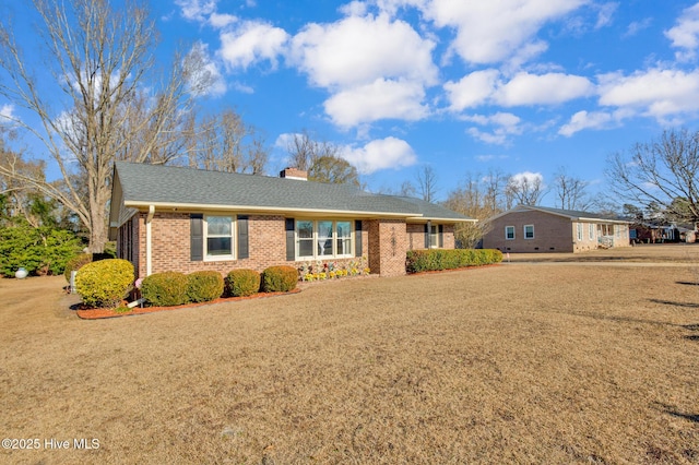 single story home featuring a shingled roof, brick siding, a chimney, and a front lawn