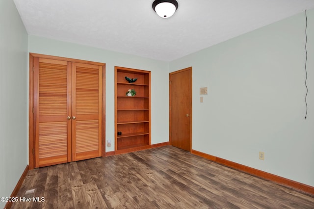 unfurnished bedroom with a textured ceiling, a closet, dark wood-style floors, and baseboards