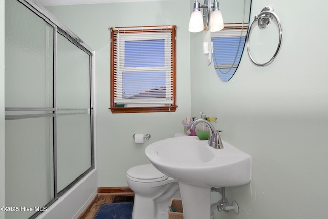 full bath with combined bath / shower with glass door, wood finished floors, toilet, and baseboards