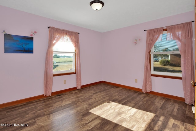 empty room featuring wood finished floors, visible vents, and baseboards