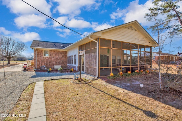 rear view of property with a sunroom, a lawn, and brick siding