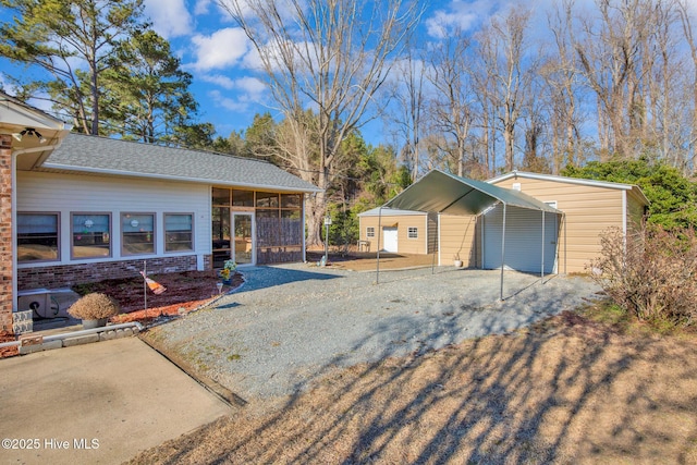 view of front of property featuring a carport, brick siding, a detached garage, and a sunroom