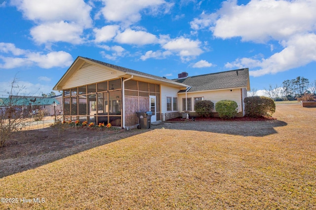 back of house featuring a lawn, a chimney, and a sunroom