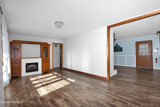 unfurnished living room with a fireplace, a textured ceiling, baseboards, and wood finished floors