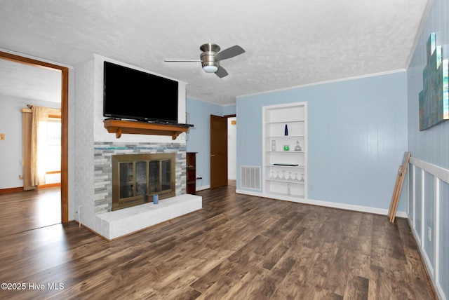 unfurnished living room featuring built in features, dark wood finished floors, visible vents, a glass covered fireplace, and a textured ceiling