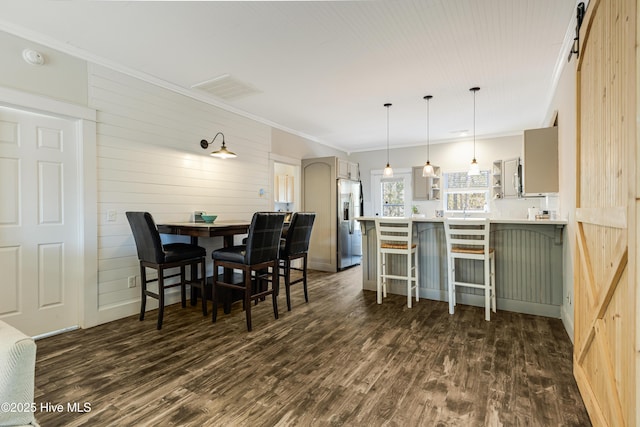 dining room with a barn door, visible vents, ornamental molding, and dark wood finished floors