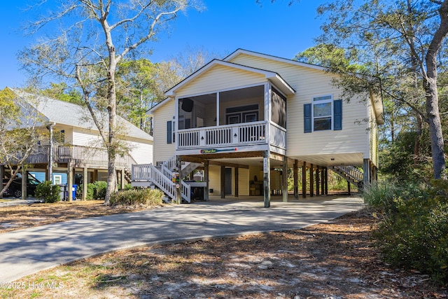 beach home featuring stairs, a carport, concrete driveway, and a sunroom