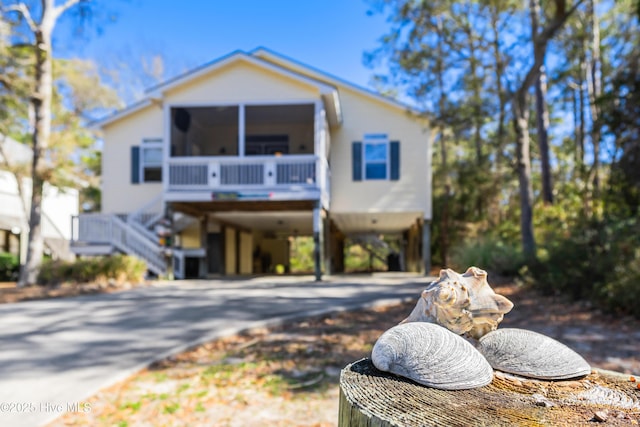 coastal home with a carport, stairway, concrete driveway, and a sunroom