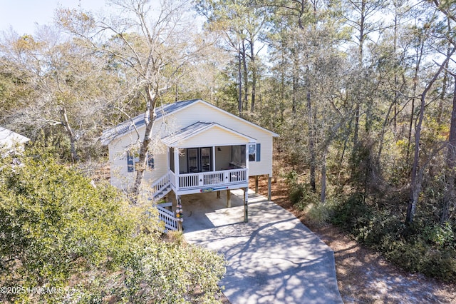 view of front of home featuring stairs, driveway, a porch, and a forest view