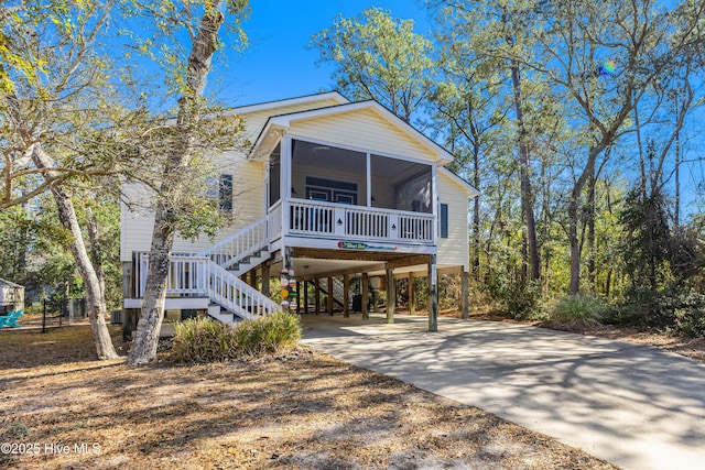 coastal home with a sunroom, stairs, a carport, and concrete driveway