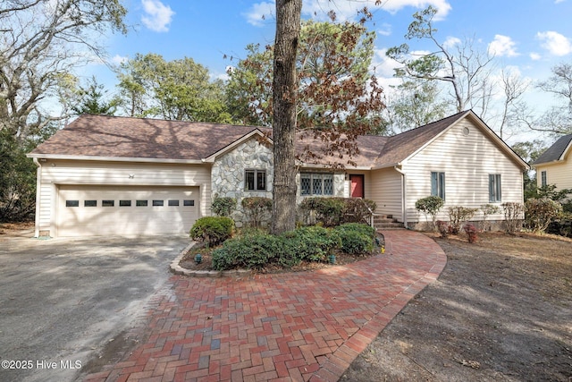 ranch-style house featuring a garage, stone siding, decorative driveway, and roof with shingles