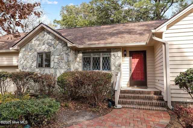 view of exterior entry featuring stone siding and a shingled roof