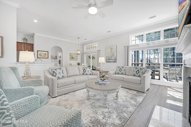 living room featuring arched walkways, crown molding, visible vents, a ceiling fan, and wood finished floors