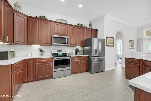 kitchen with arched walkways, crown molding, light countertops, decorative backsplash, and appliances with stainless steel finishes