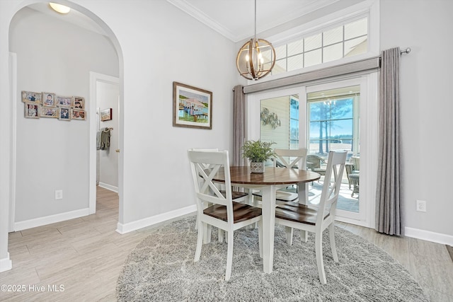 dining space featuring arched walkways, an inviting chandelier, ornamental molding, light wood-type flooring, and baseboards