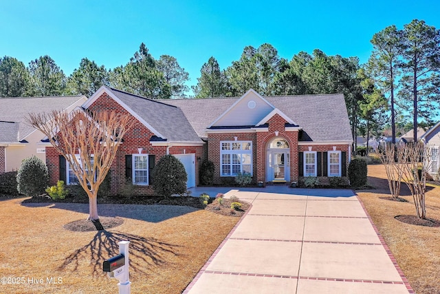 view of front of house with a shingled roof, a front lawn, concrete driveway, and brick siding