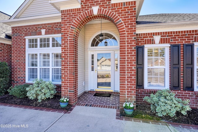 view of exterior entry featuring brick siding and roof with shingles