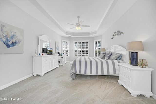 bedroom with light colored carpet, a ceiling fan, baseboards, a tray ceiling, and crown molding