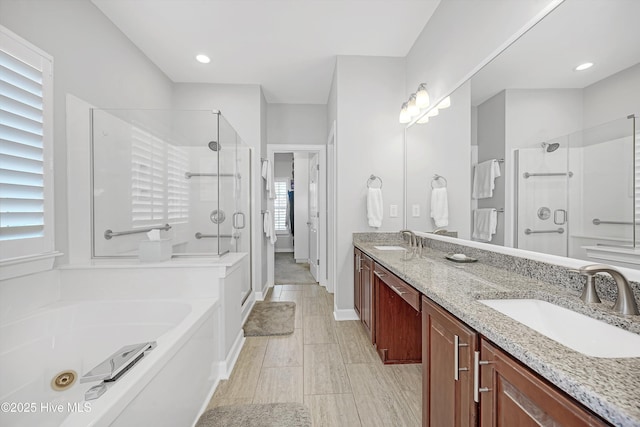 full bath featuring a stall shower, double vanity, a sink, and a bath