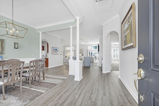 foyer entrance featuring decorative columns, arched walkways, wood finished floors, and ornamental molding