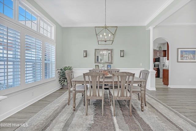 dining area featuring arched walkways, wood finished floors, ornamental molding, decorative columns, and an inviting chandelier