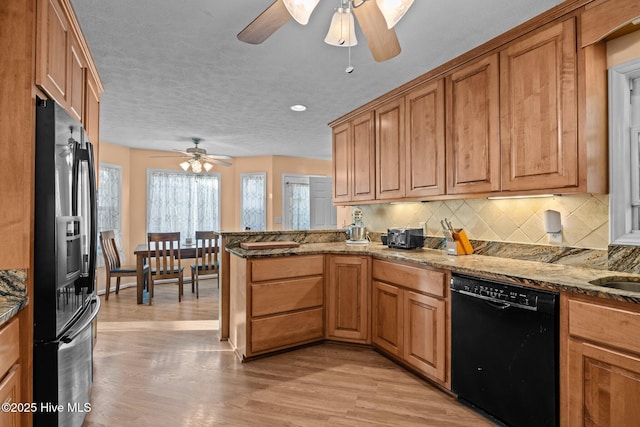 kitchen featuring backsplash, stone countertops, light wood-type flooring, a peninsula, and black appliances