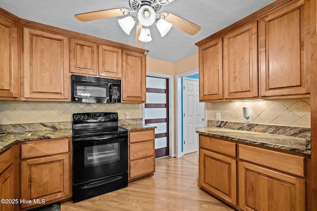 kitchen with dark stone countertops, brown cabinets, light wood finished floors, and black appliances