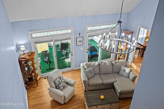 living room featuring vaulted ceiling, baseboards, wood finished floors, and an inviting chandelier