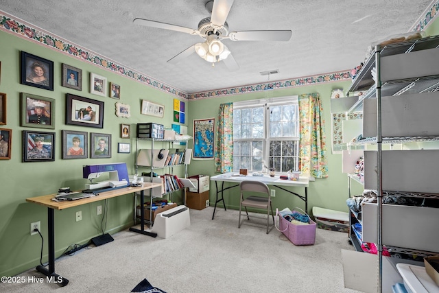 carpeted office with a textured ceiling, baseboards, visible vents, and a ceiling fan