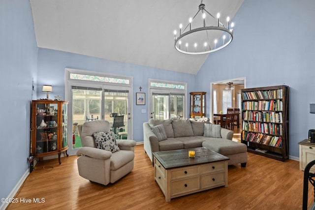 living area with light wood-style floors, a notable chandelier, high vaulted ceiling, and baseboards