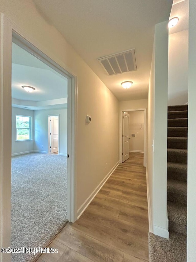 hallway with carpet floors, visible vents, wood finished floors, baseboards, and stairs