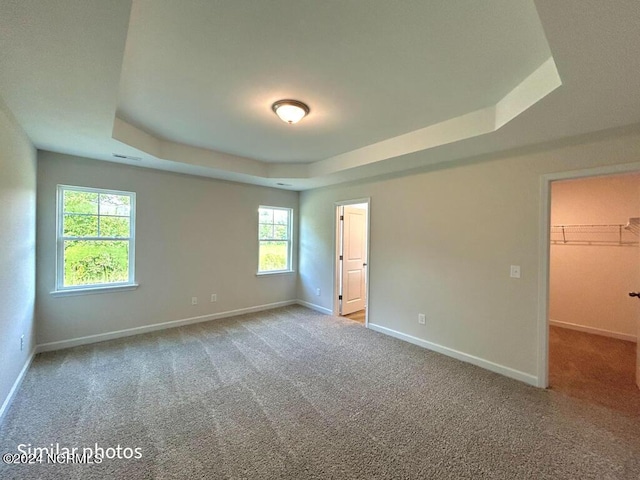 unfurnished bedroom featuring visible vents, baseboards, a raised ceiling, carpet, and a walk in closet