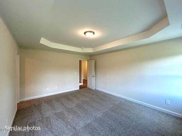 empty room featuring a tray ceiling, dark carpet, baseboards, and a skylight