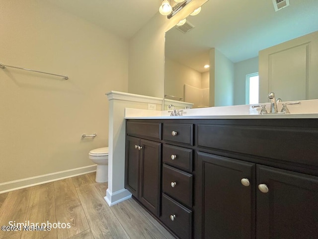 bathroom featuring double vanity, visible vents, a sink, wood finished floors, and baseboards