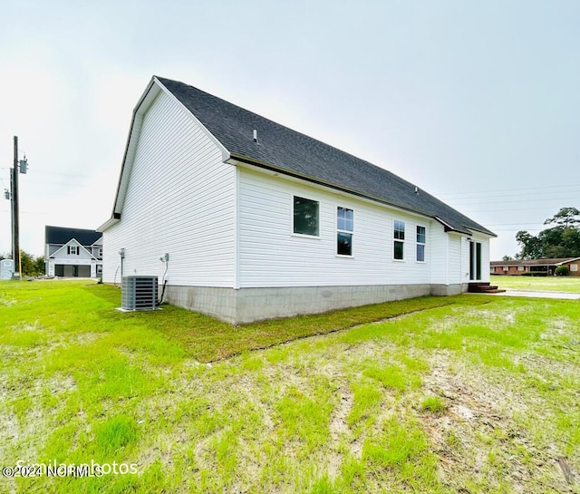 view of home's exterior featuring roof with shingles, central AC, and a yard