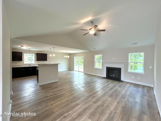 unfurnished living room featuring visible vents, a fireplace with flush hearth, wood finished floors, baseboards, and ceiling fan with notable chandelier