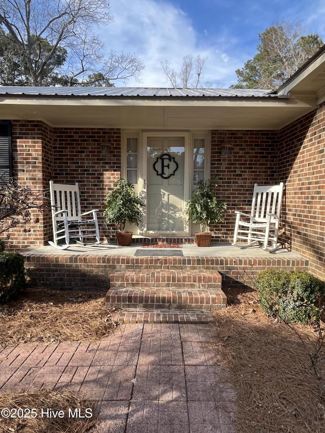 property entrance featuring brick siding, a porch, and metal roof