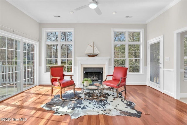 living area with visible vents, baseboards, wood-type flooring, ornamental molding, and a fireplace